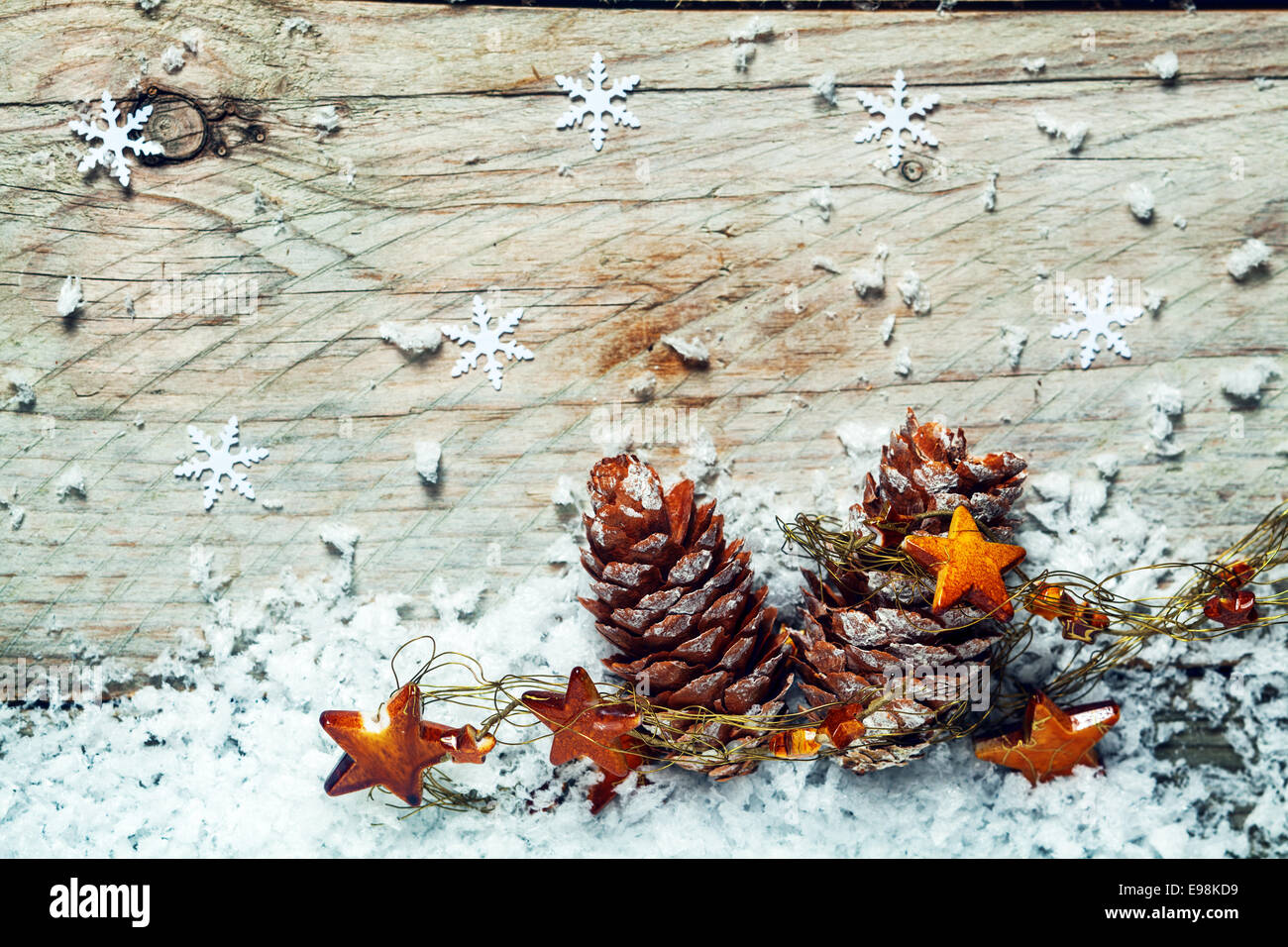 Christmas Noel background with dried pine cones draped in a garland of stars nestling on cold winter snow with a wooden background with snowflake decorations and copyspace Stock Photo