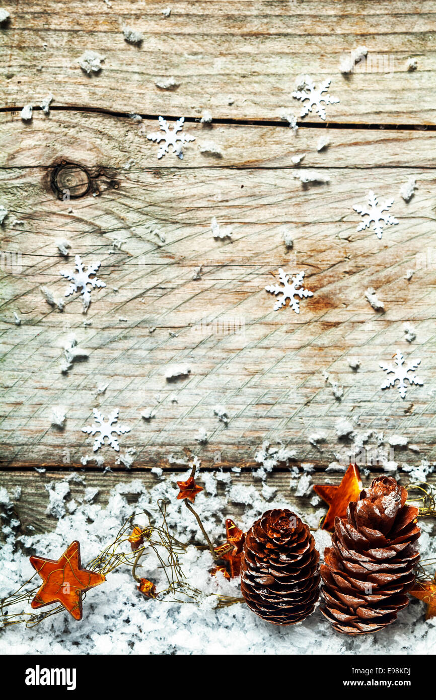 Christmas country background with a garland of decorative golden orange stars draped over pine cones in snow below a textured wooden background with snowflake decorations and copyspace Stock Photo