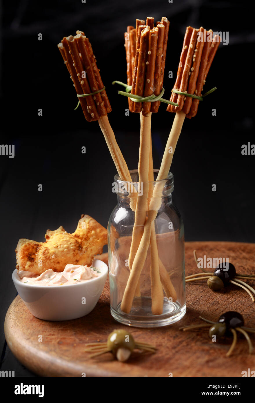 Creative Halloween snacks and appetizers with witches broomsticks made from bread sticks and pretzels with creepy spiders of olives and spaghetti on a table at a Halloween celebration Stock Photo