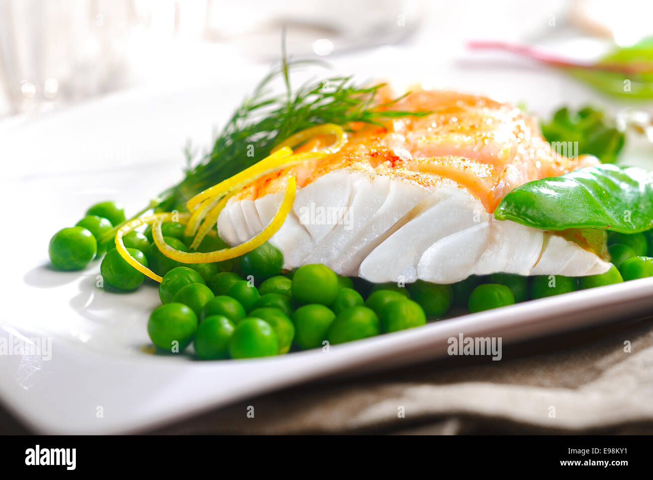 Delicious oven baked fish or grilled fillet or steak with peas, a mangetout pod, lemon zest and fresh dill for a nutritious seafood dinner Stock Photo