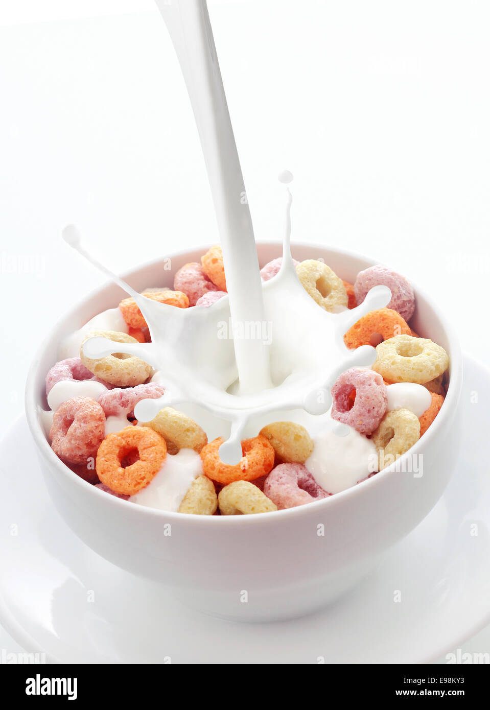 Pouring fresh creamy milk into a bowl of colorful fruit loops breakfast cereal in a white ceramic bowl with a splash on a white Stock Photo