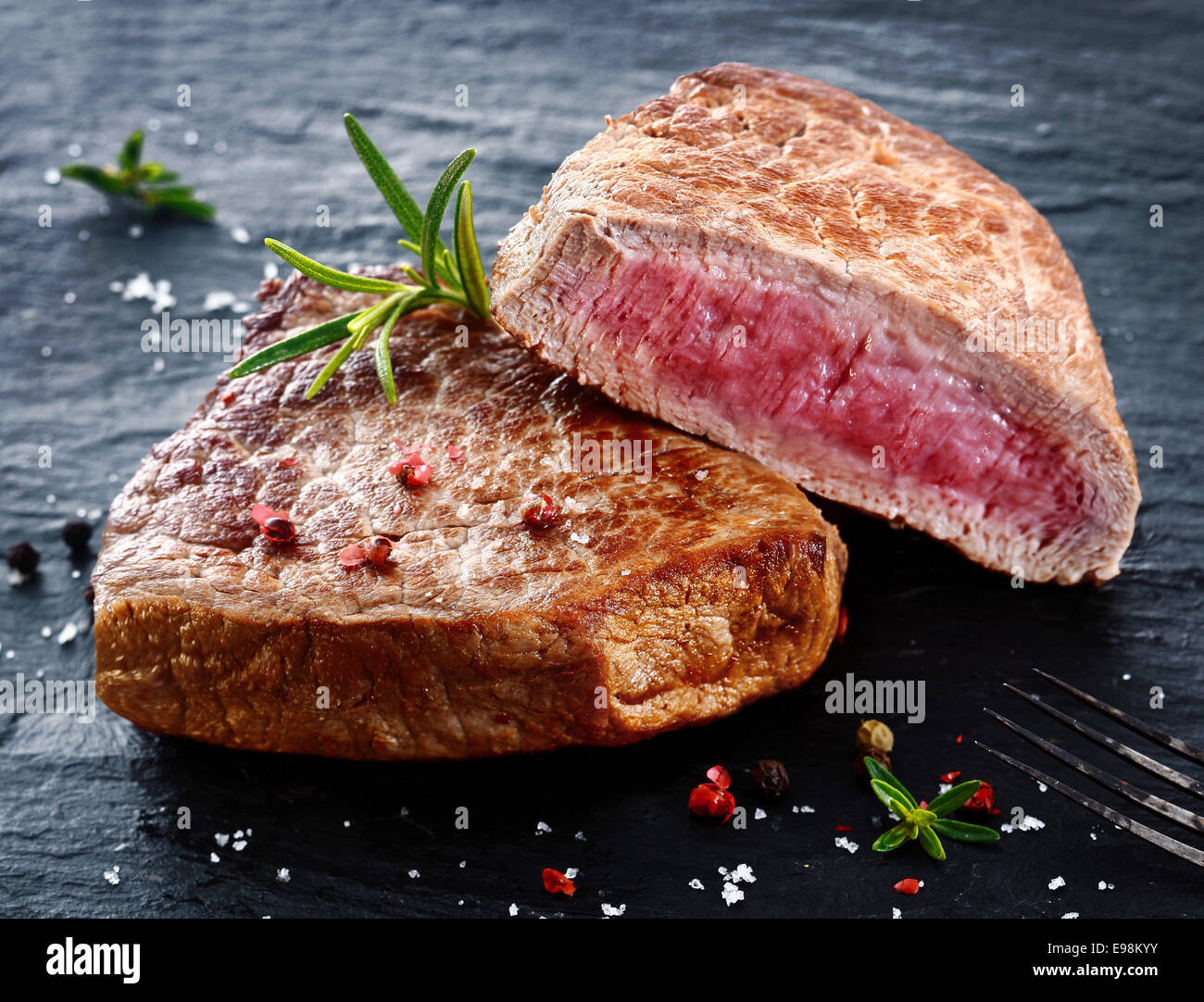 Two portions of lean trimmed grilled beef steak cut through to show the succulent tender red meat and seasoned with rosemary, salt and pepper in a steakhouse or restaurant Stock Photo