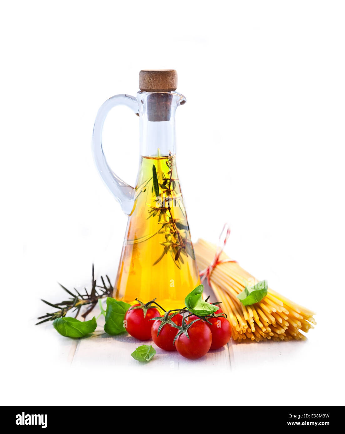 Fresh ingredients for making a spaghetti dish with a conical flask of olive oil, herbs , tomatoes and uncooked spaghetti pasta. Stock Photo