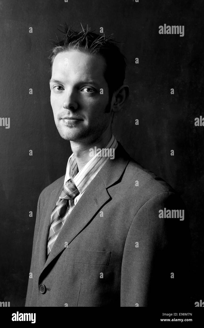 dark moody shot of a young man in a suit, shirt and tie against a black background Stock Photo