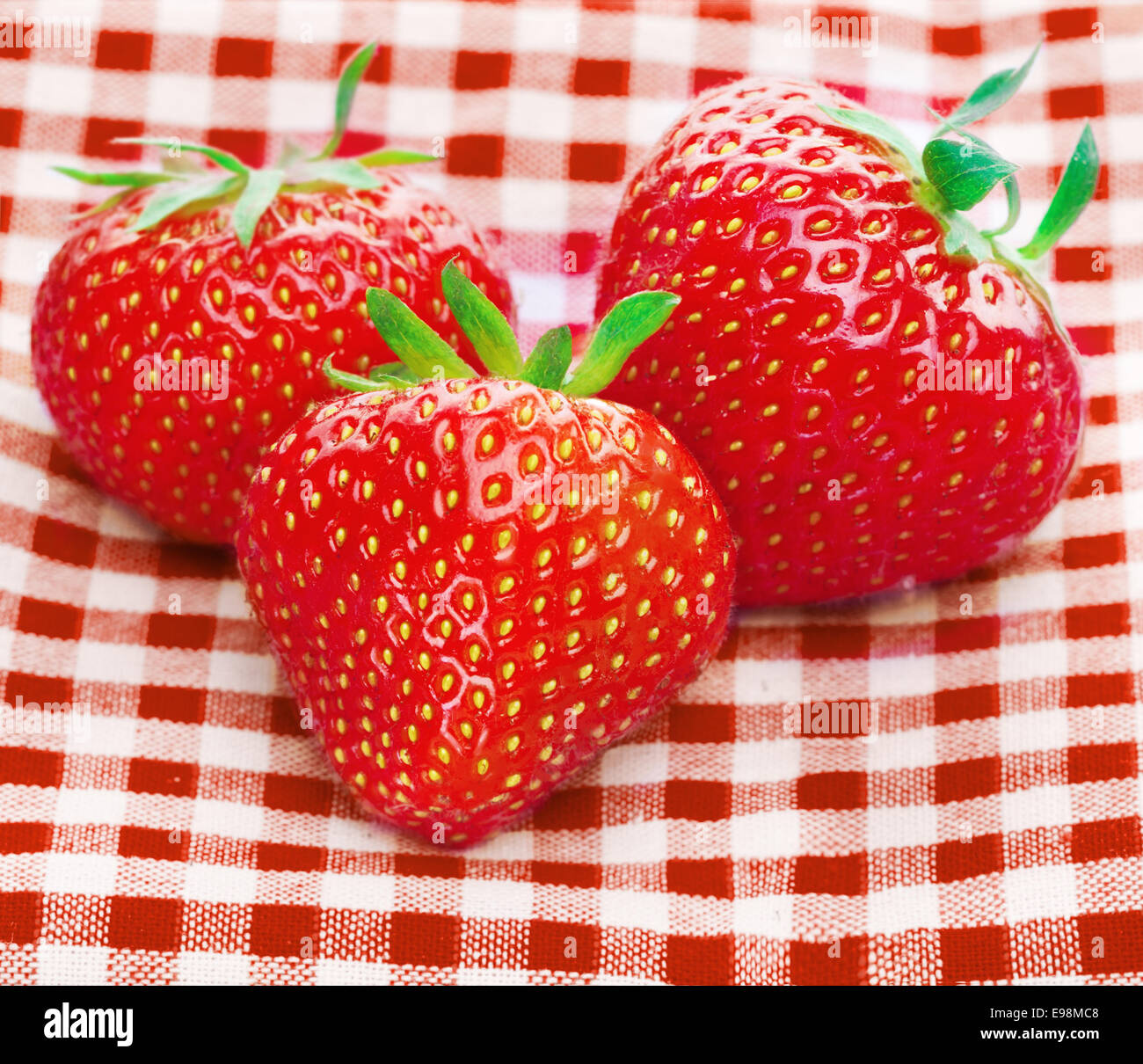 Fresh three strawberries on red plaid tablecloth Stock Photo