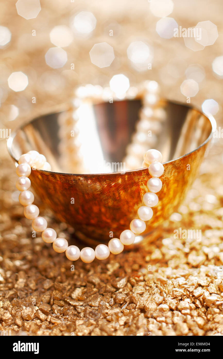 A matched string of pearls cascades down from a pretty silver bowl backed by a bokeh of festive party lights Stock Photo