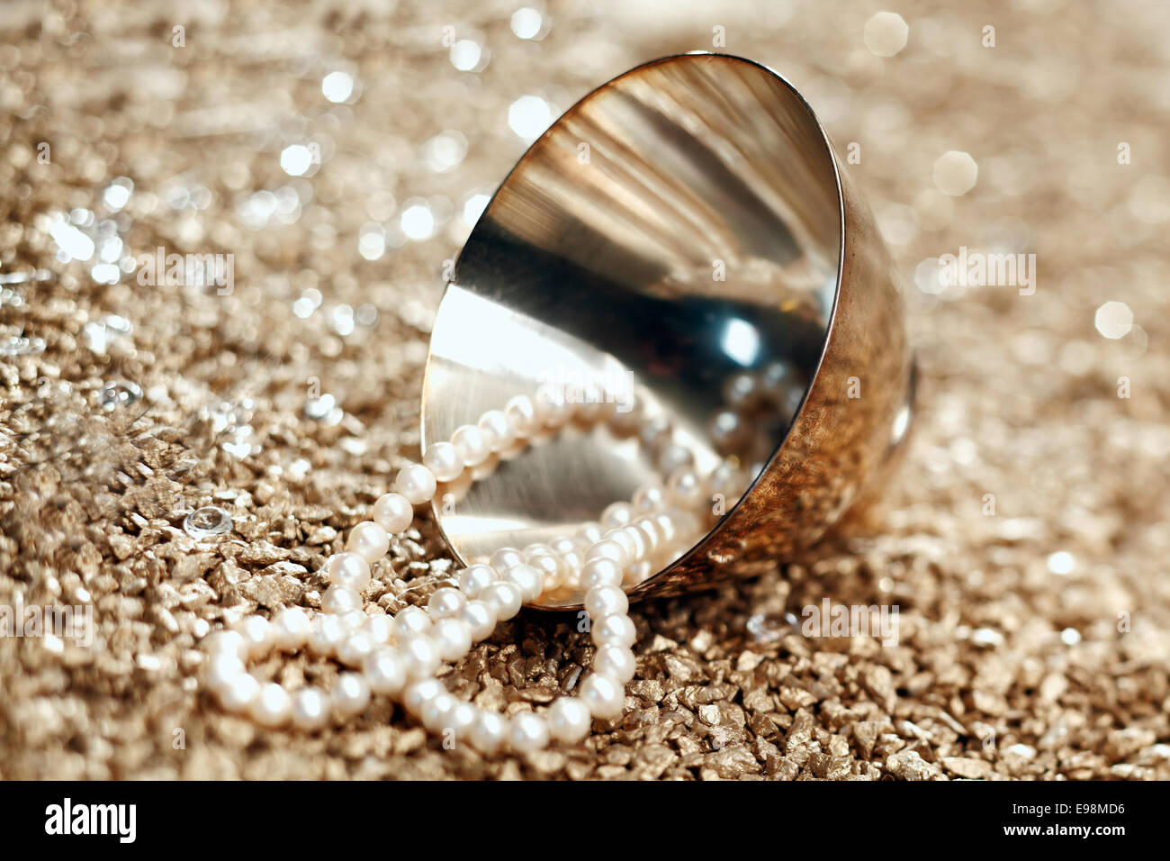 A string of matched pearls spills out of a silver bowl lying on its side with shallow depth of field Stock Photo