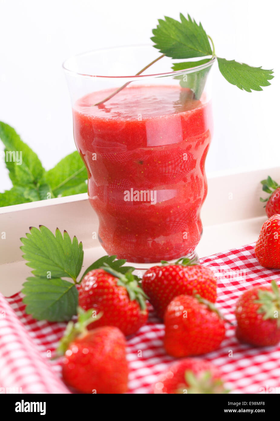 Refreshing strawberry smoothie surrounded by ripe red strawberries on a red and white checked napkin Stock Photo