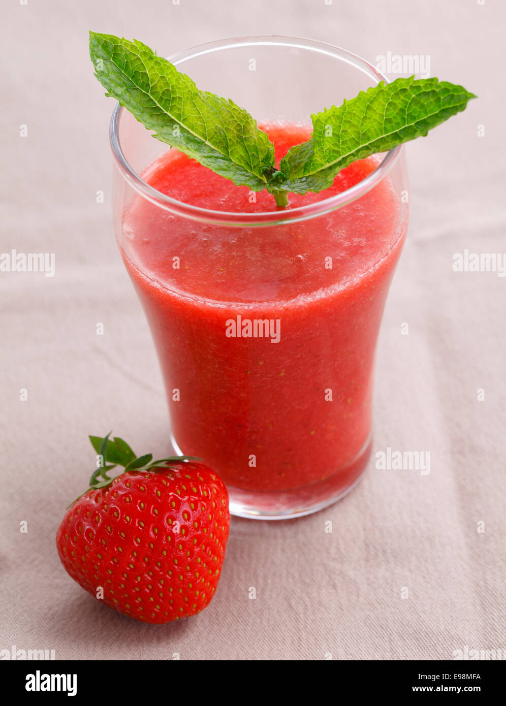 High angle view of a glass of healthy fresh strawberry smoothie and a ripe red strawberry served ready for a vegetarian breakfast Stock Photo