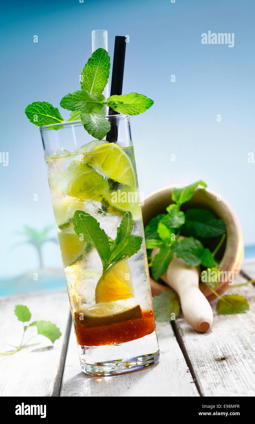 Beach Cocktail with pestle and mortar standing on a jetty in front of a blue lagoon with a palm. Stock Photo