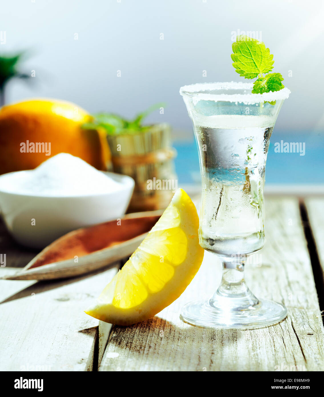 Chilled glass of vodka cocktail garnished with frosting and mint and served with lemon alongside a turquoise pool Stock Photo