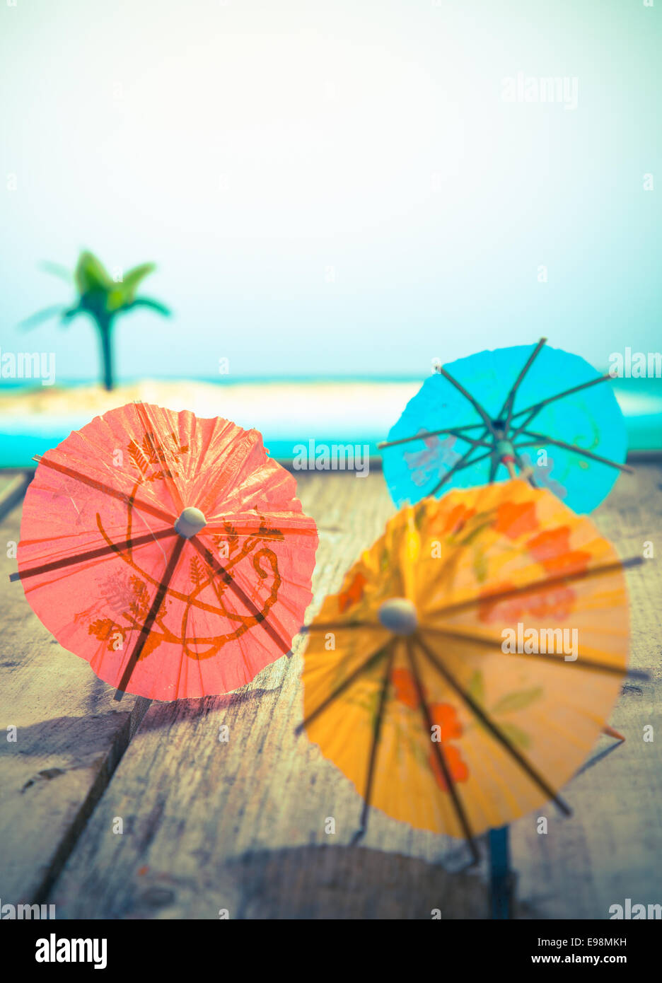 Colourful cocktail or paper umbrellas lying on a wooden deck with a tropical seaside backdrop, conceptual for partying and festivity Stock Photo