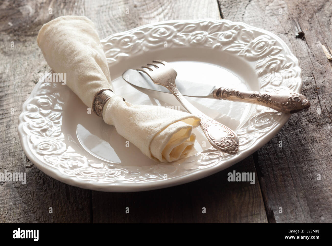 White rose patterned dinner plate with silverware and a napkin in an informal table setting Stock Photo