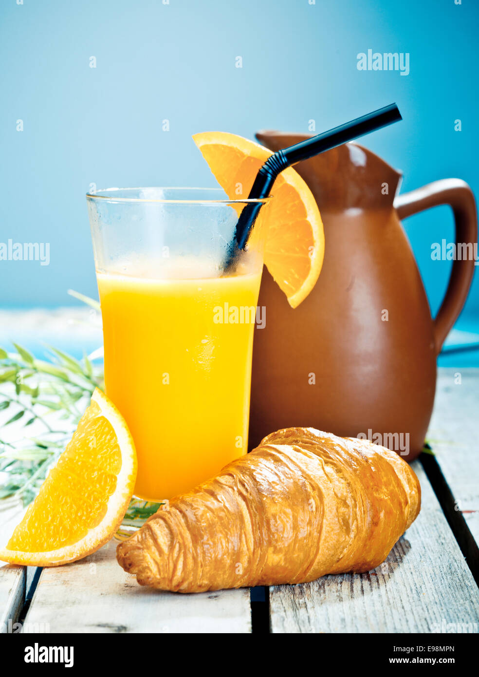 Healthy tropical breakfast consisting of a chilled glass of freshly squeezed orange juice and a crisp croissant on a deck overlooking th sea Stock Photo