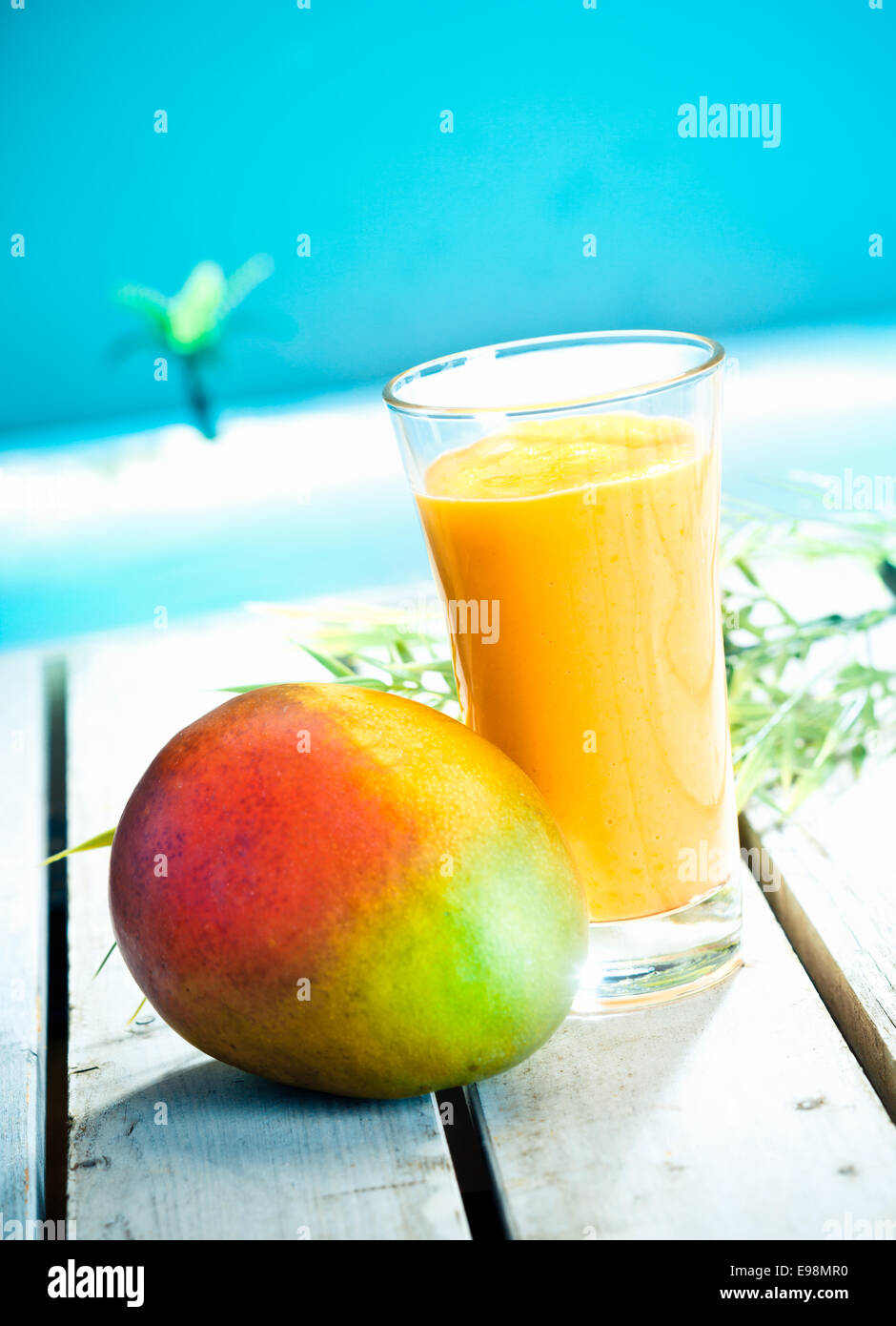Creamy mango smoothie with blended fresh mango juice and yoghurt served overlooking a tropical ocean Stock Photo