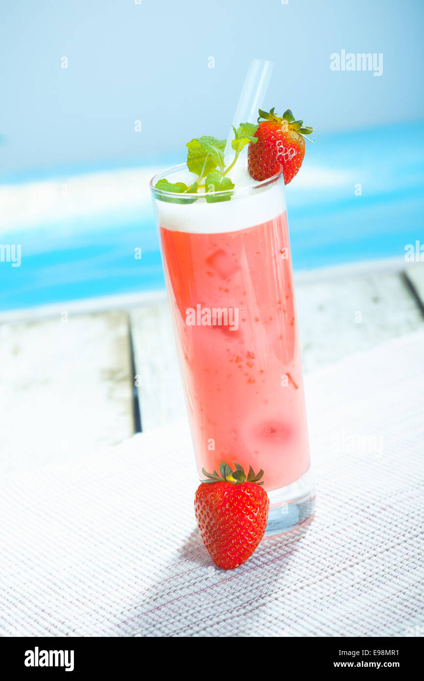 Scrumptious chilled glass of yoghurt and strawberry smoothie served on a deck overlooking the sea Stock Photo