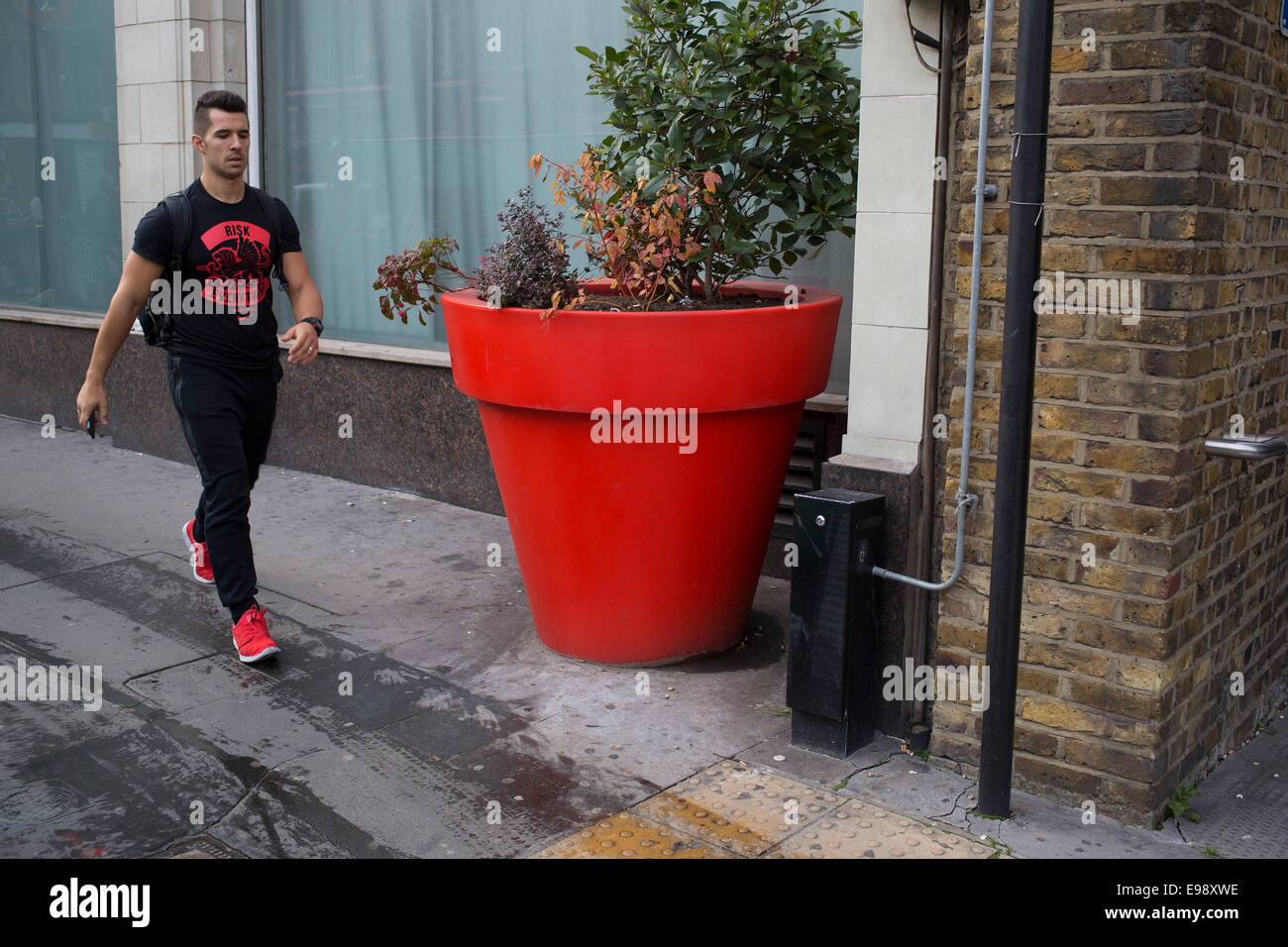 People on the streets interact with a large red plant pot in the City of London, UK. This situation creates a weird scale. Stock Photo