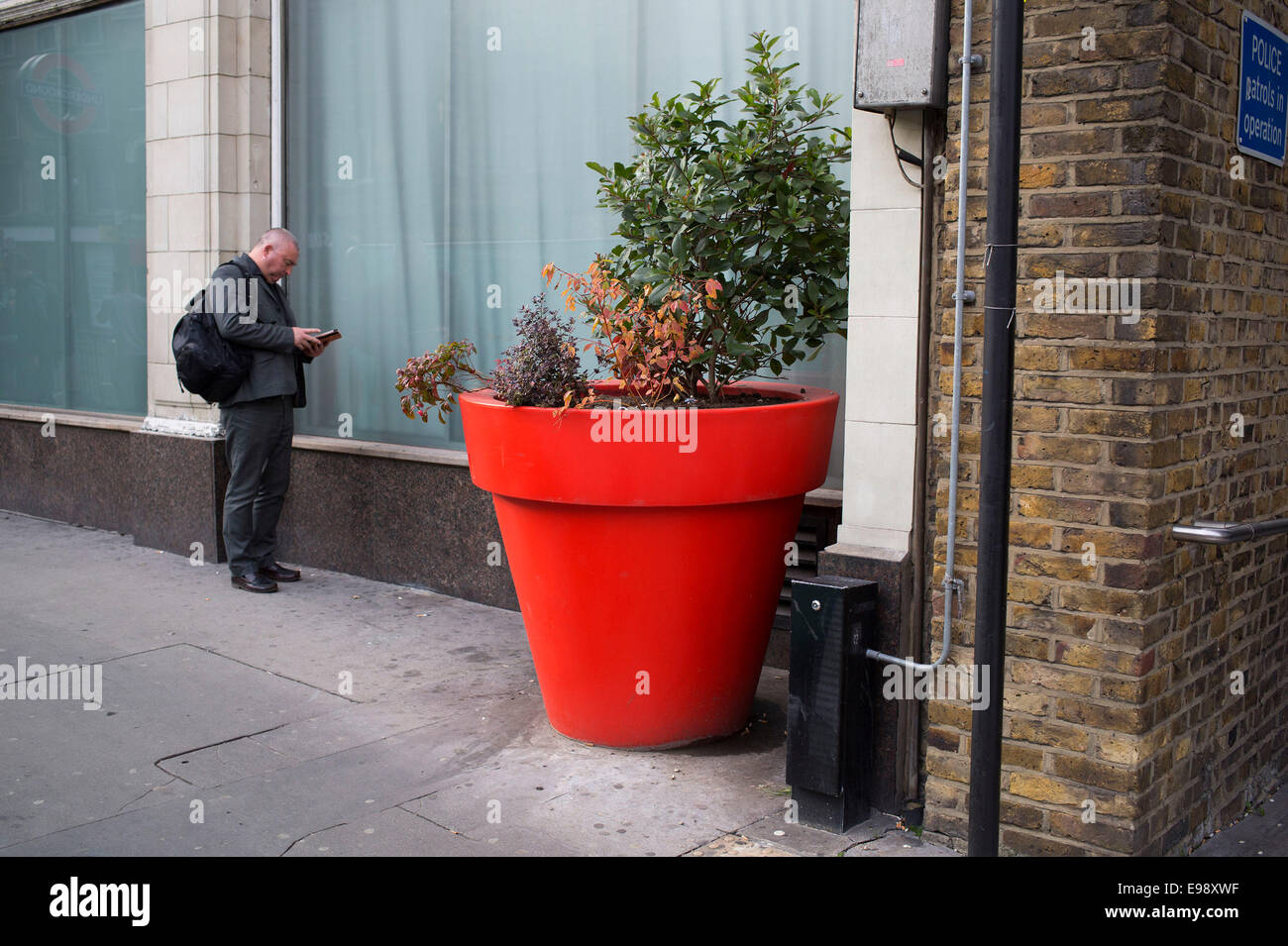 People on the streets interact with a large red plant pot in the City of London, UK. This situation creates a weird scale. Stock Photo