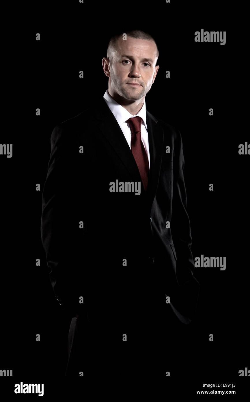 male fitness instructor with shaved head in a suit shot against a black background, Stock Photo