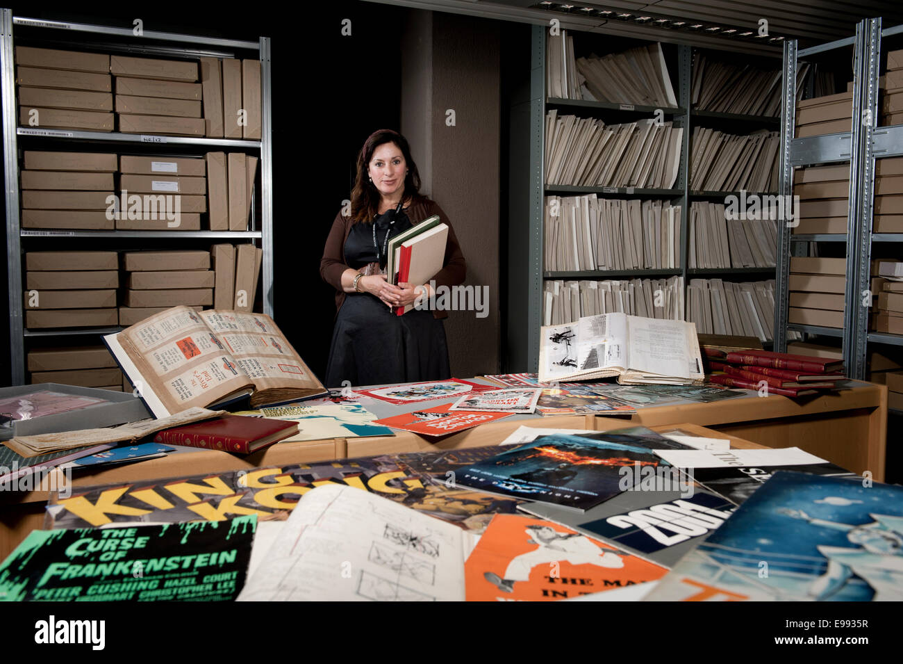 female member of staff at the BFI archive with storage shelves filled with archival boxes holding all kinds of film memorabilia Stock Photo
