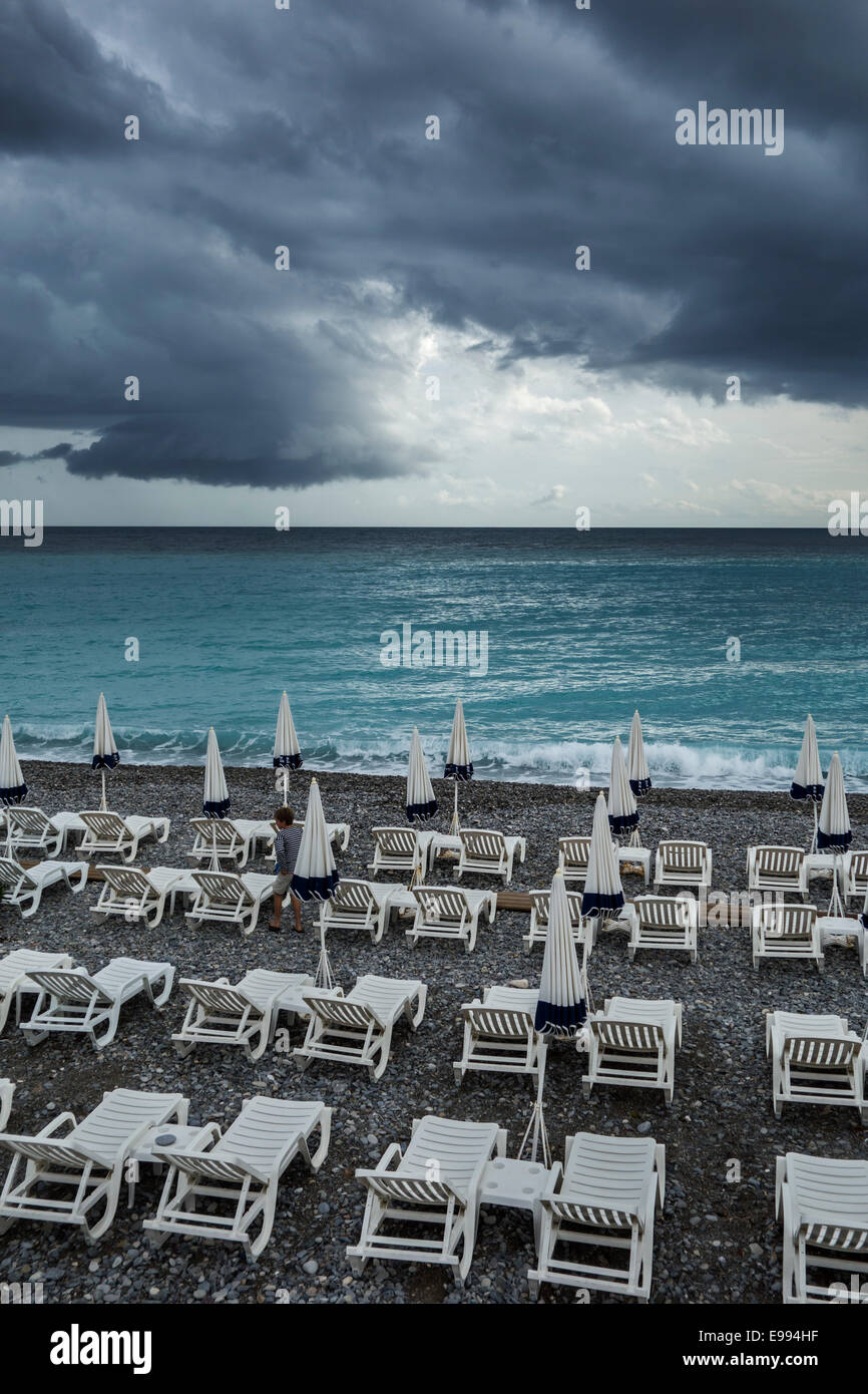 White reclining chairs on deserted beach during bad weather with dark, menacing rain clouds over the sea Stock Photo