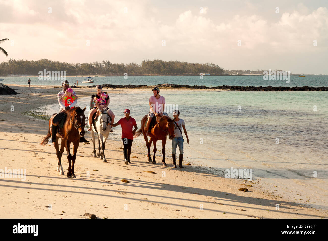 A family riding horses on the beach at sunset, Belle Mare Beach, Mauritius Stock Photo