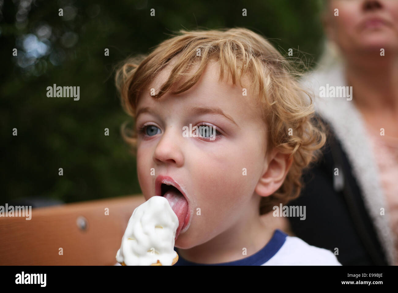 little boy eating ice cream with mum in background Stock Photo