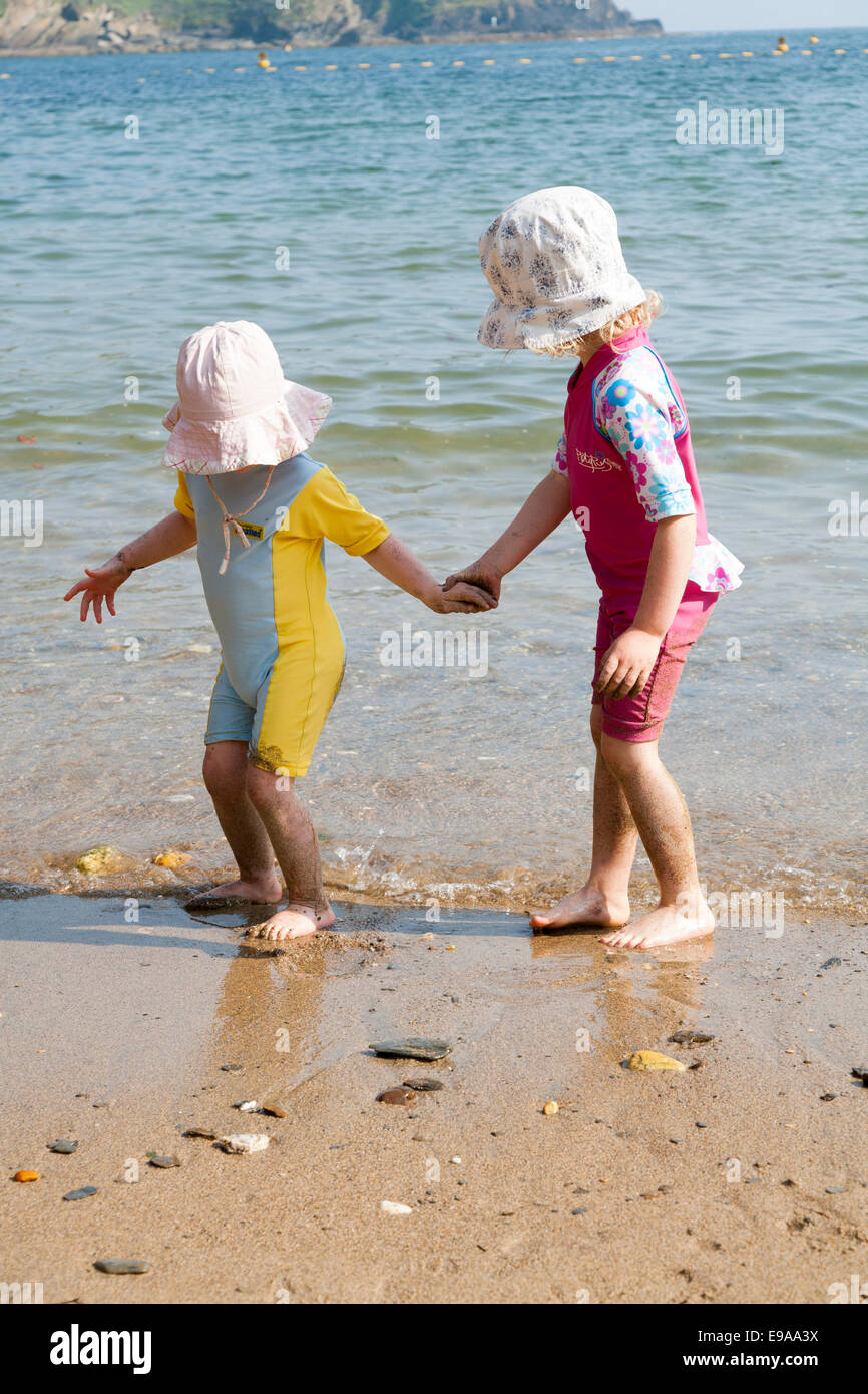 Two little girls / toddlers walk on a sandy beach and paddle in the sea