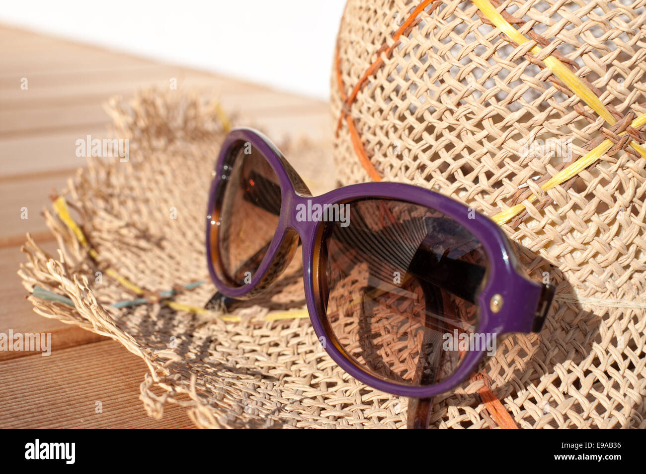 Straw sun hat and purple sunglasses on cedar deck Stock Photo