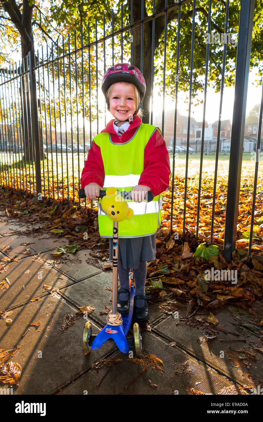 Child / girl on scooter in hi vis / high visibility vest jacket scootering / going to Reception class on a scooter at sunrise UK Stock Photo