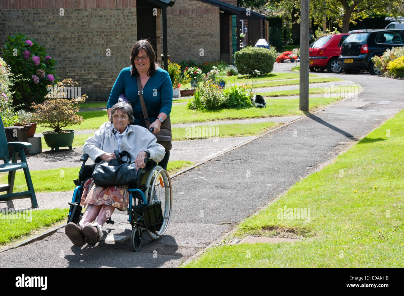 An elderly lady is pushed in a wheelchair by her carer or assistant back to her home in sheltered accommodation. Stock Photo