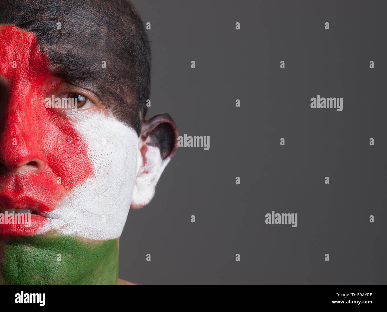 Sad man and his face painted with palestine flag. The man is isolated on dark background. Stock Photo