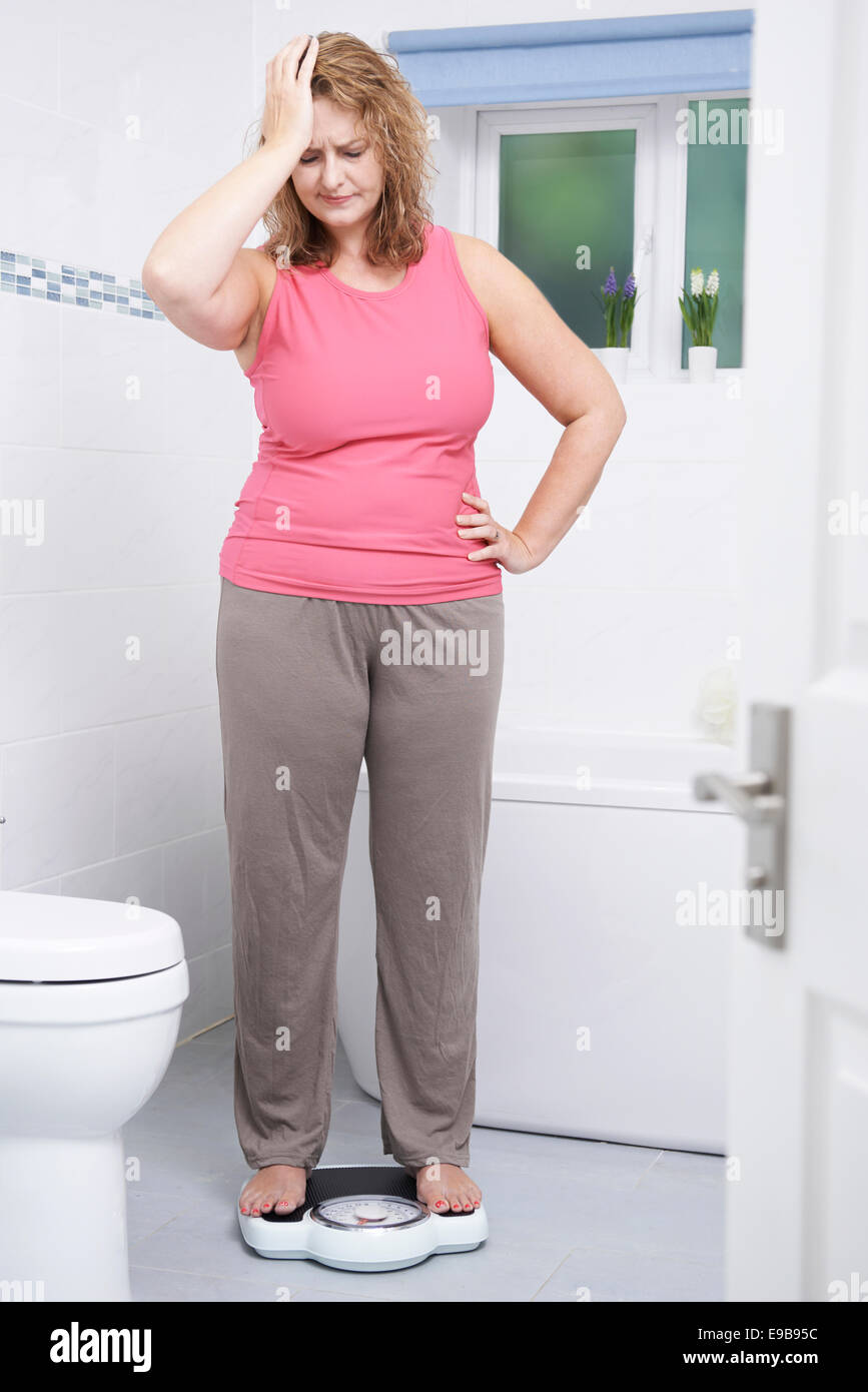 Overweight Woman Weighing Herself On Scales In Bathroom Stock Photo