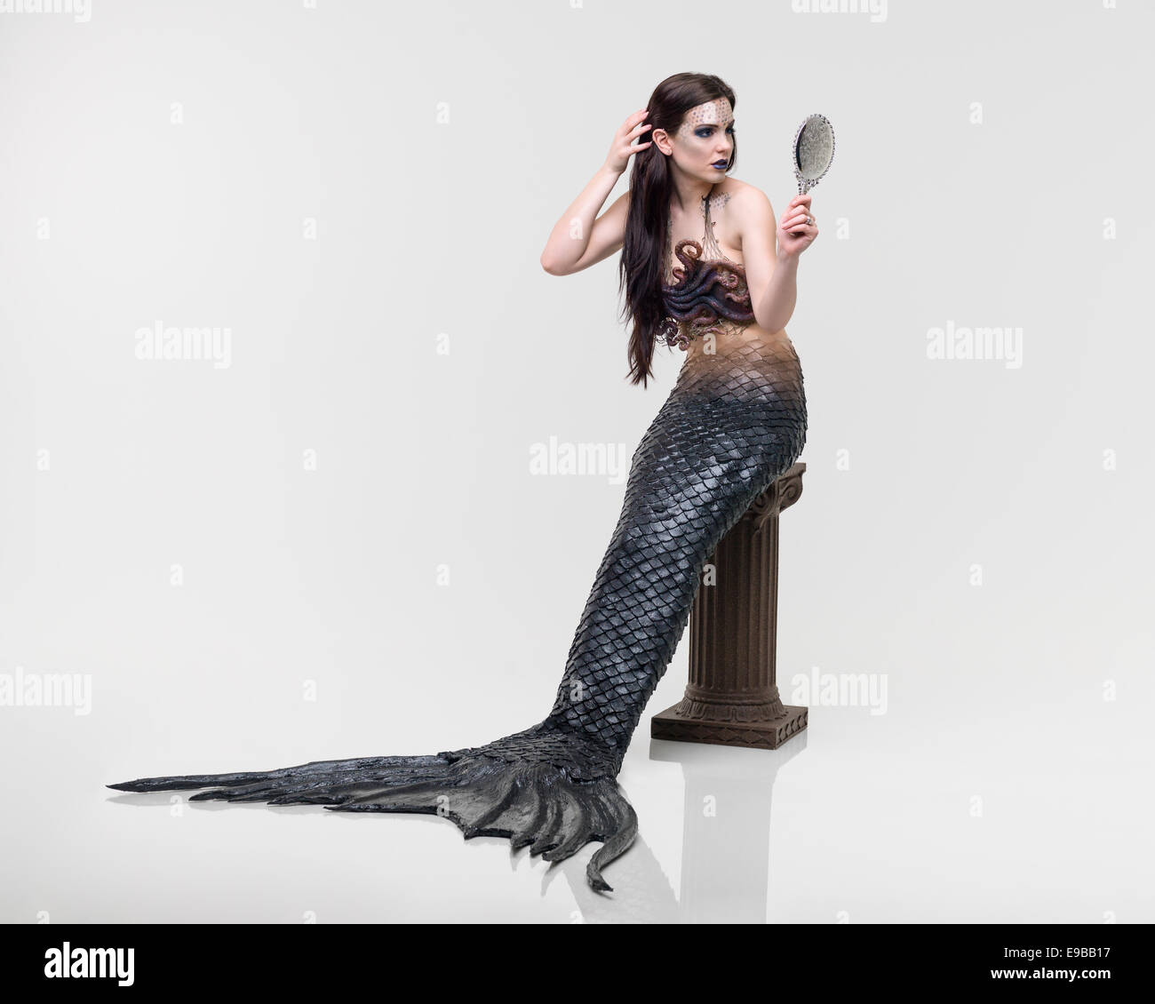 Evil mermaid looking at herself in a hand mirror sitting on a podium in Virginia Beach, Virginia Stock Photo