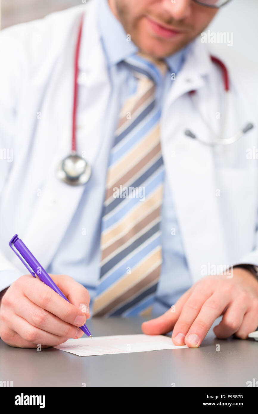 Young doctor writing medical prescription in surgery at desk Stock Photo