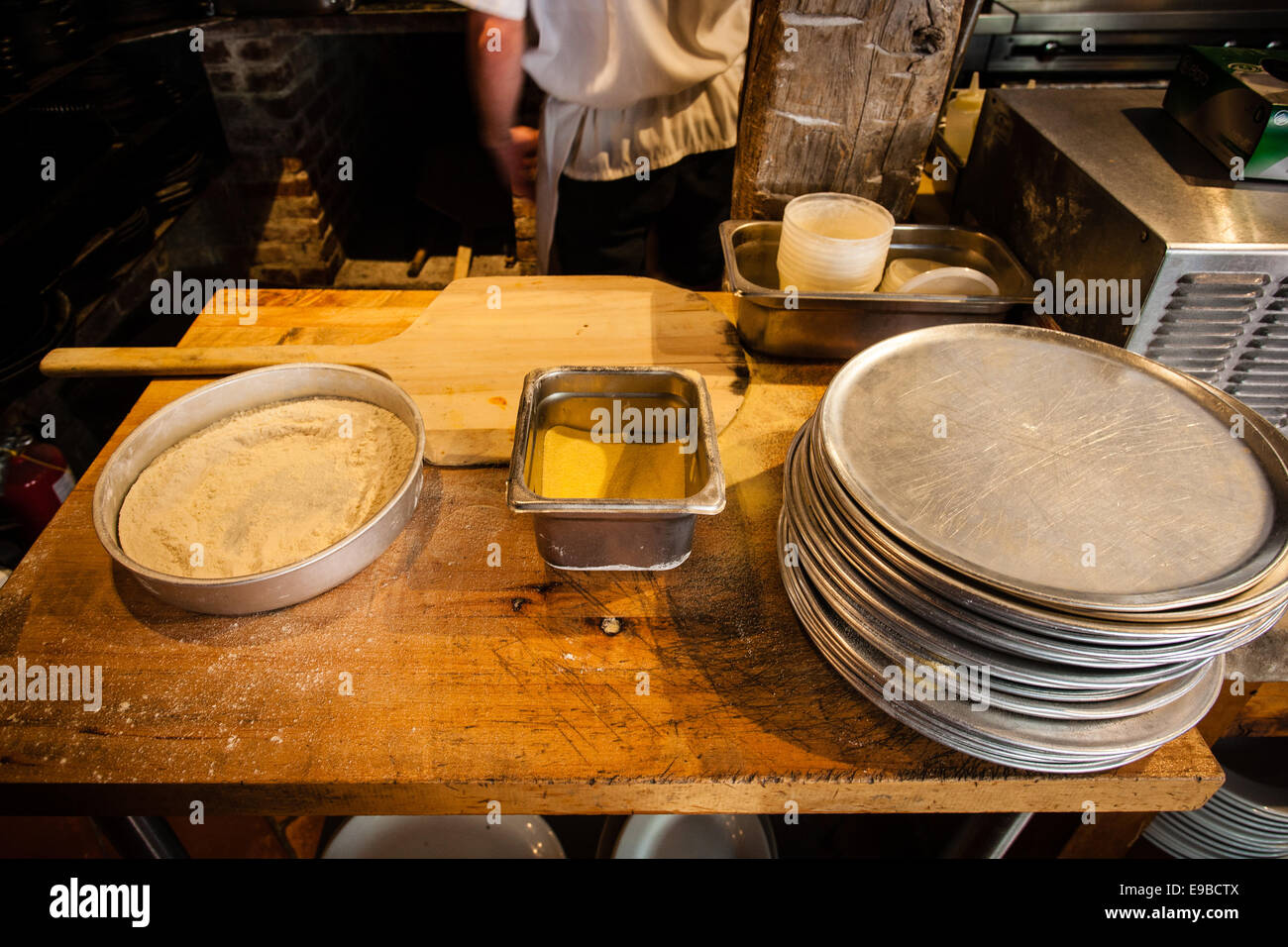 Work table of a pizza maker in front of brick oven showing pizza ingredients and tools. Stock Photo