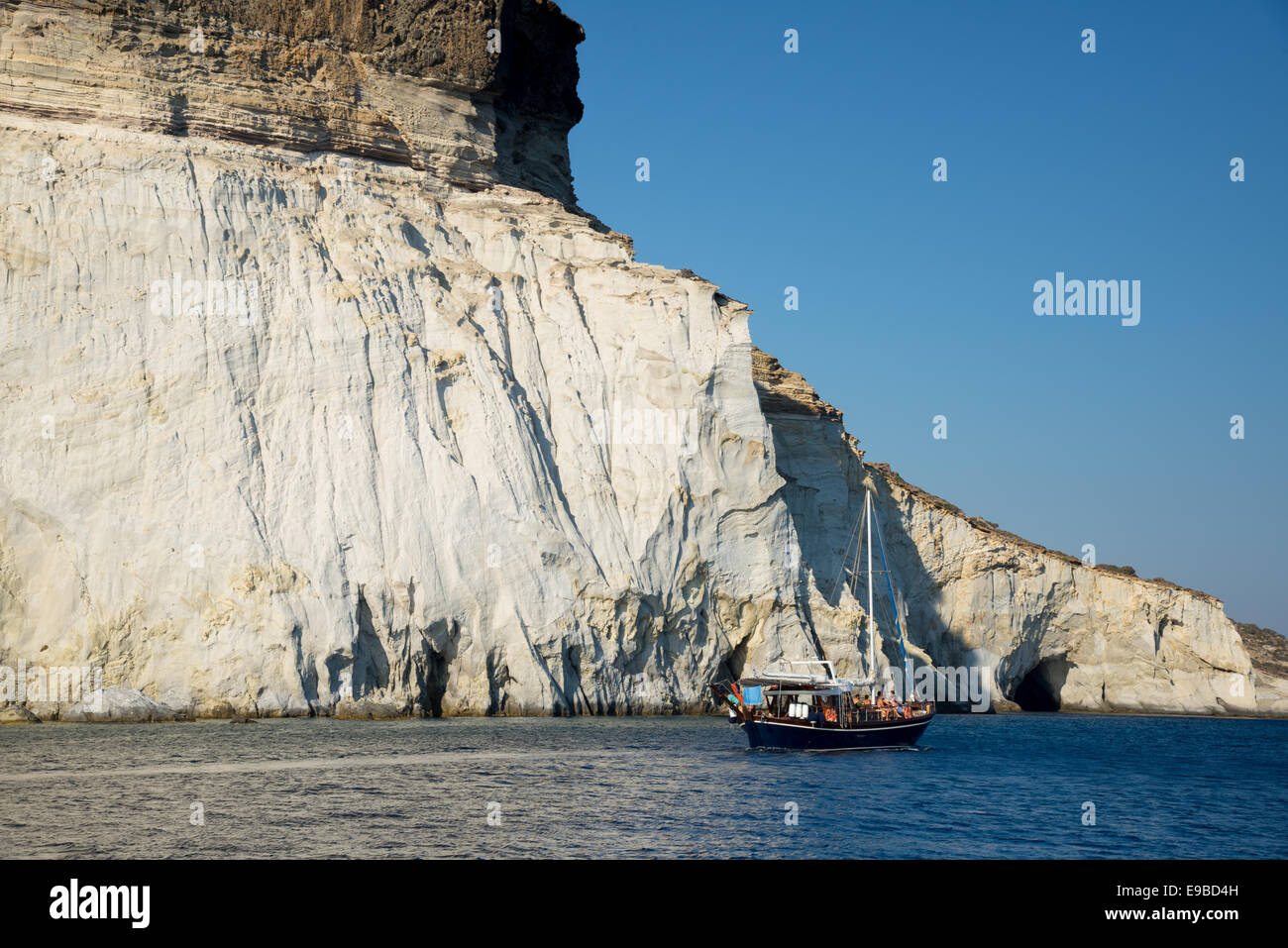boat alongside the white cliffs of gerontas at milos in greece Stock Photo