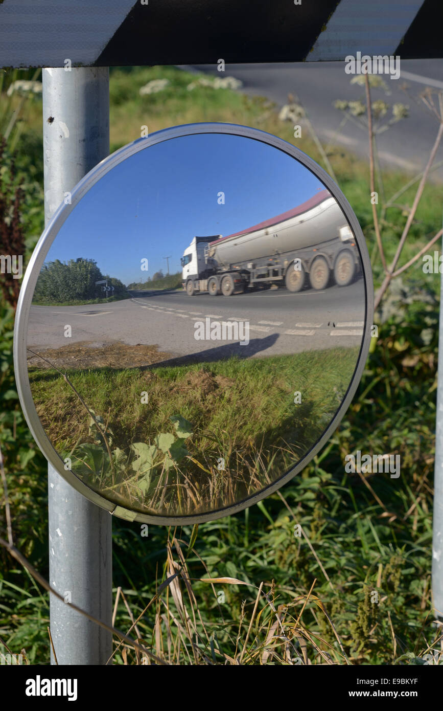 lorry passing warning sign of sharp bend and circular safety mirror to give drivers emerging from junction view of road uk Stock Photo