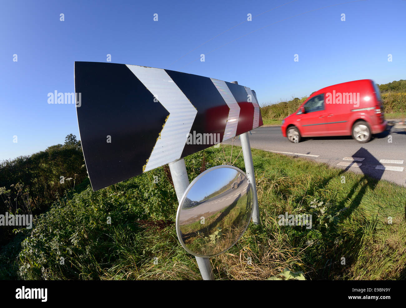 van passing warning sign of sharp bend and circular safety mirror to give drivers emerging from junction view of road uk Stock Photo