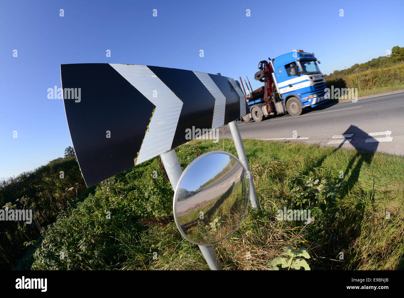 lorry passing warning sign of sharp bend and circular safety mirror to give drivers emerging from junction view of road uk Stock Photo
