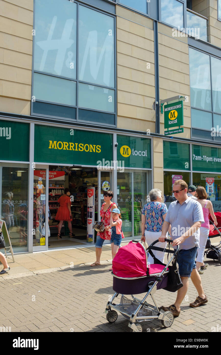 Shoppers on a busy York street in front of a Morrisons Morrison's Local convenience store. Stock Photo