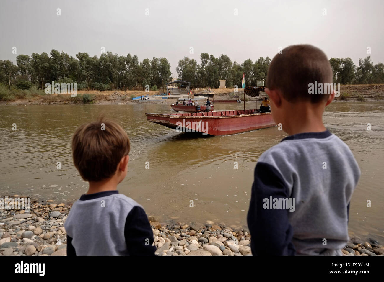 Kurdish boys looking from the Syrian side of Faysh Khabur or Fishkhabur - Semalka border crossing  at boats crossing the Tigris river from Iraq’s Kurdistan region into Syria’s northeastern Kurdish area Stock Photo