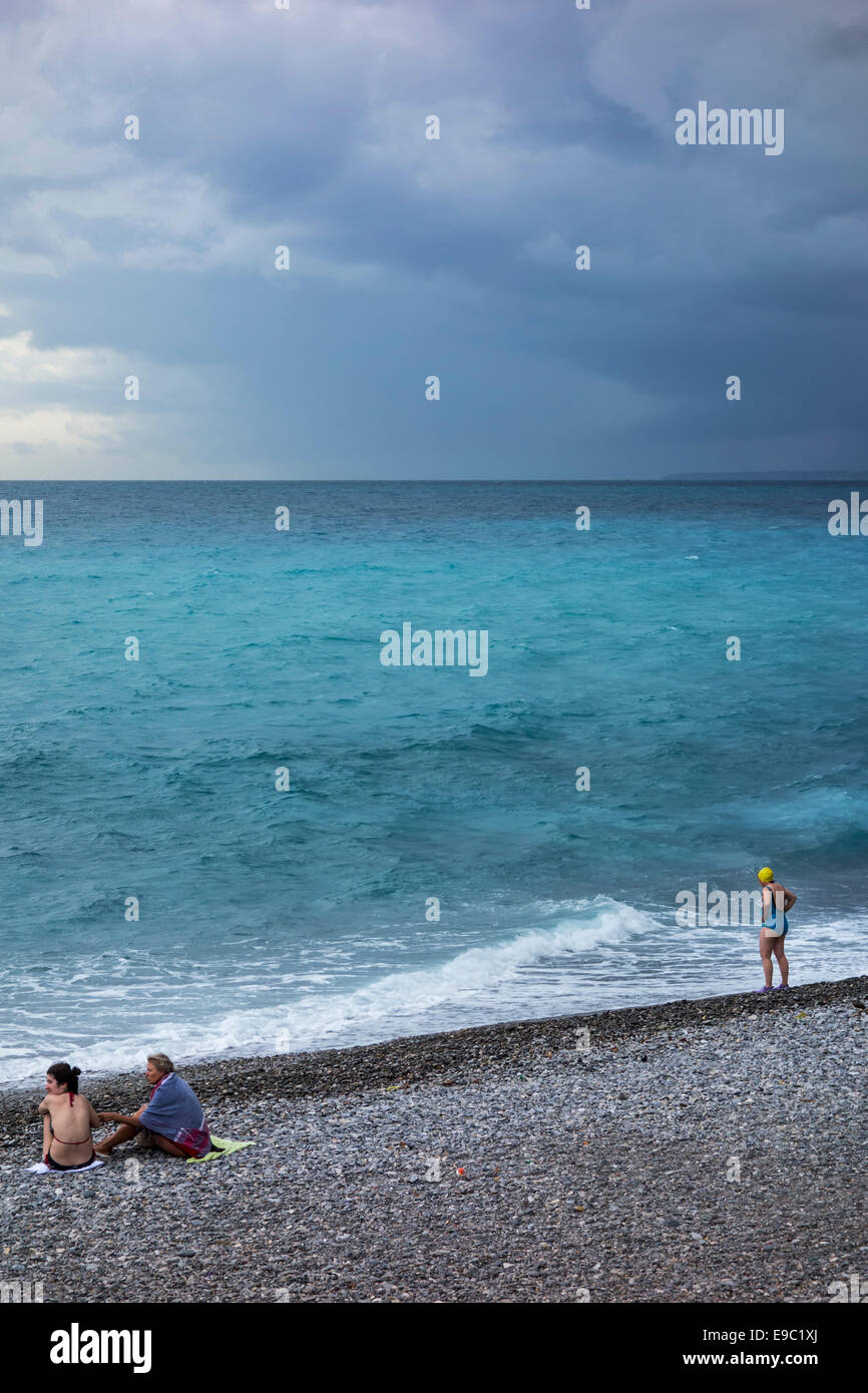 Female swimmers on shingle beach during bad weather with rainstorm approaching over the sea Stock Photo