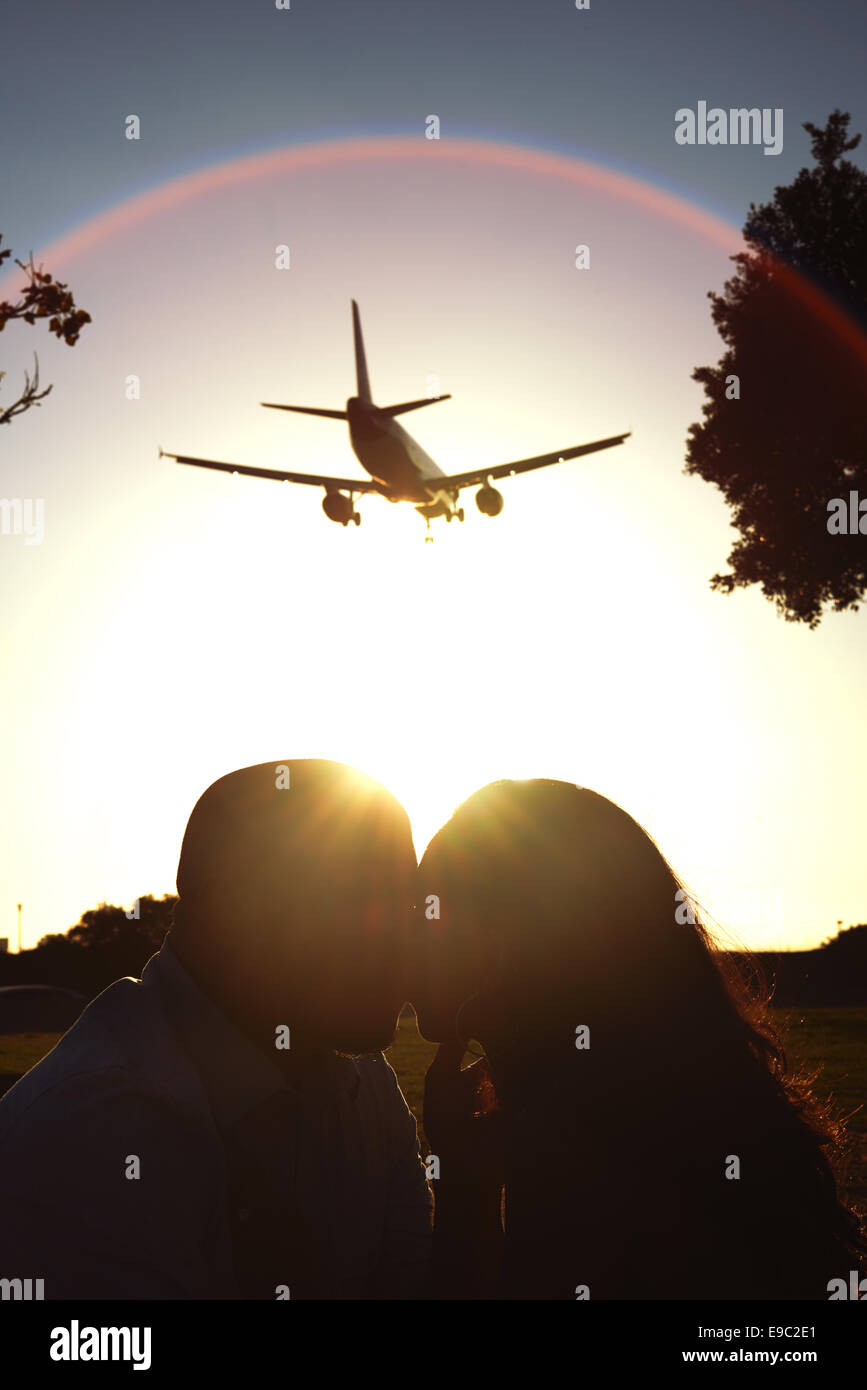 Couple kissing with sun behind them and a airplane flying overhead Stock Photo