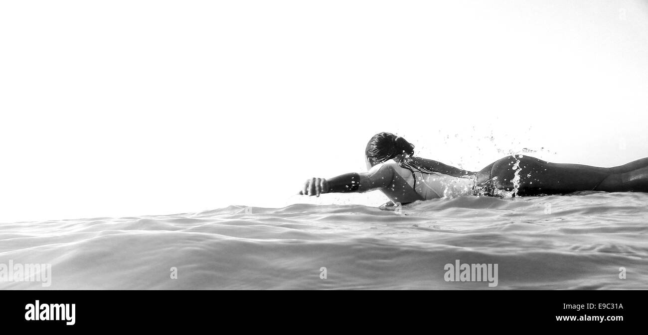 Surfer girl paddling out into the ocean in black and white Stock Photo