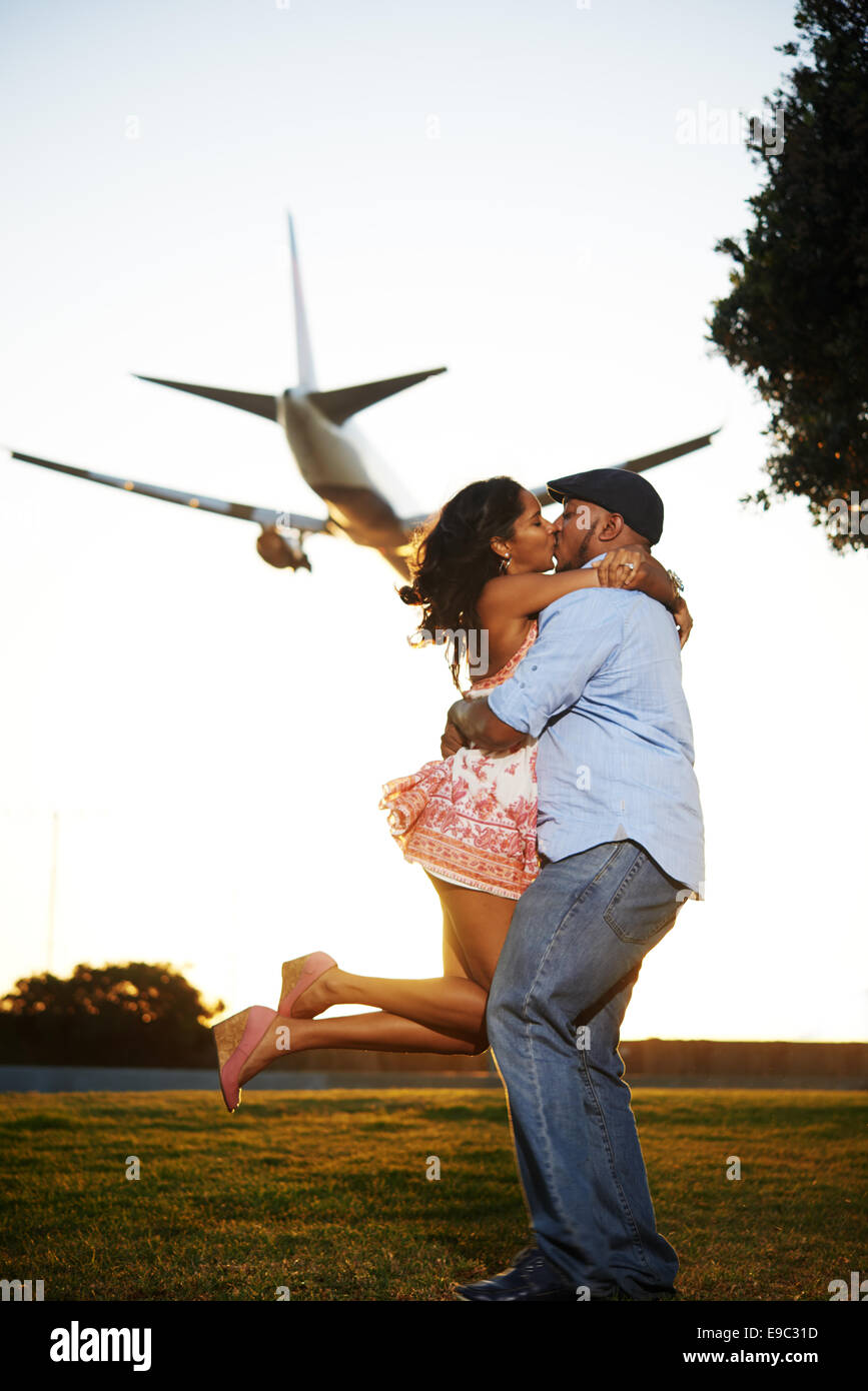 Couple kissing while the guy holds up the girl and a plane is flying overhead Stock Photo