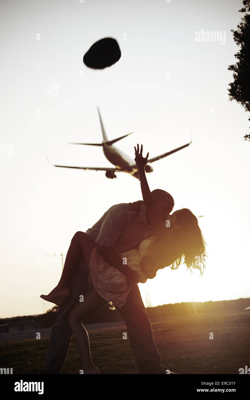 Couple dip kissing while a plane flies by during sunset Stock Photo