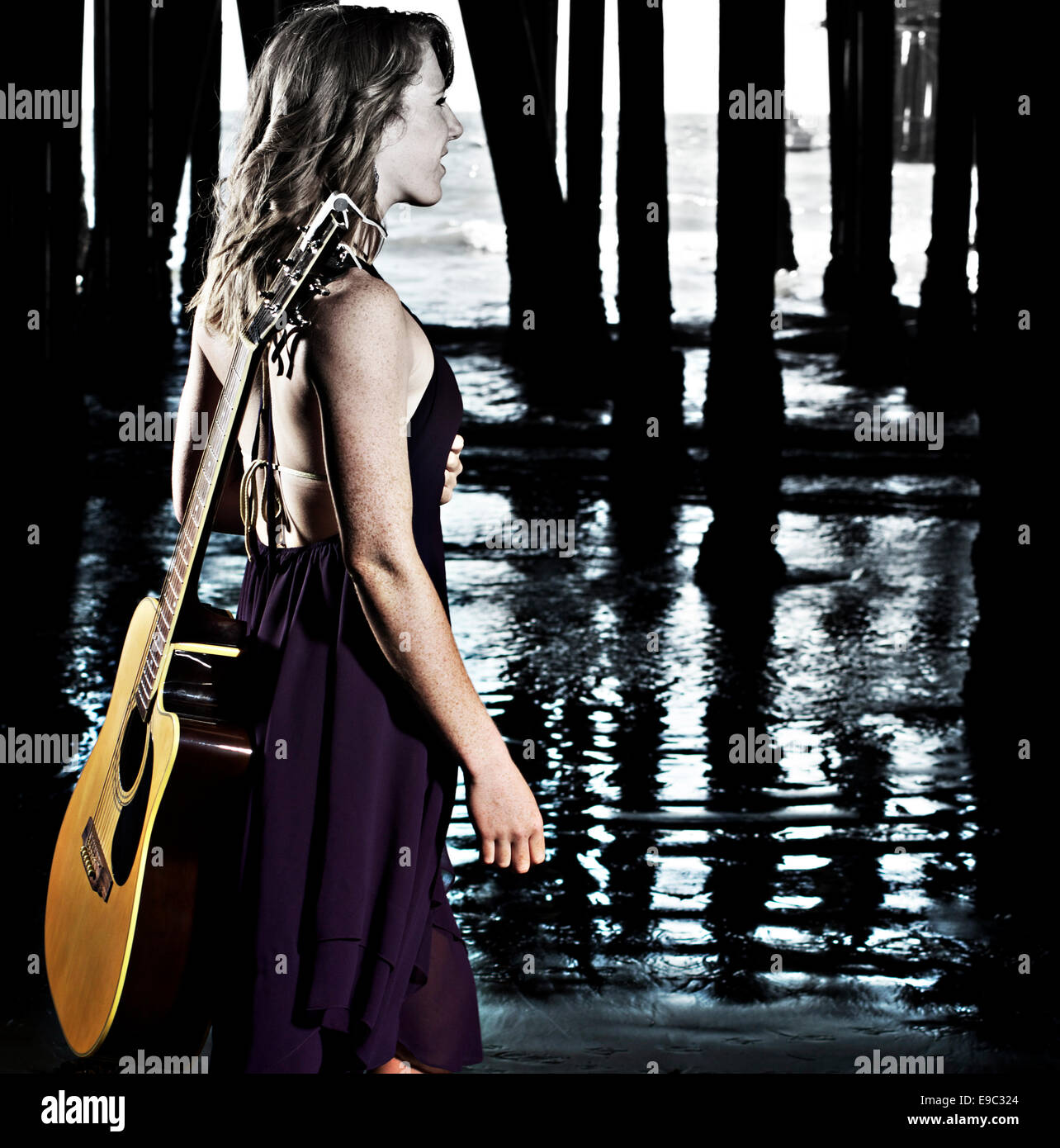 Girl in dress under pier with guitar looking away Stock Photo