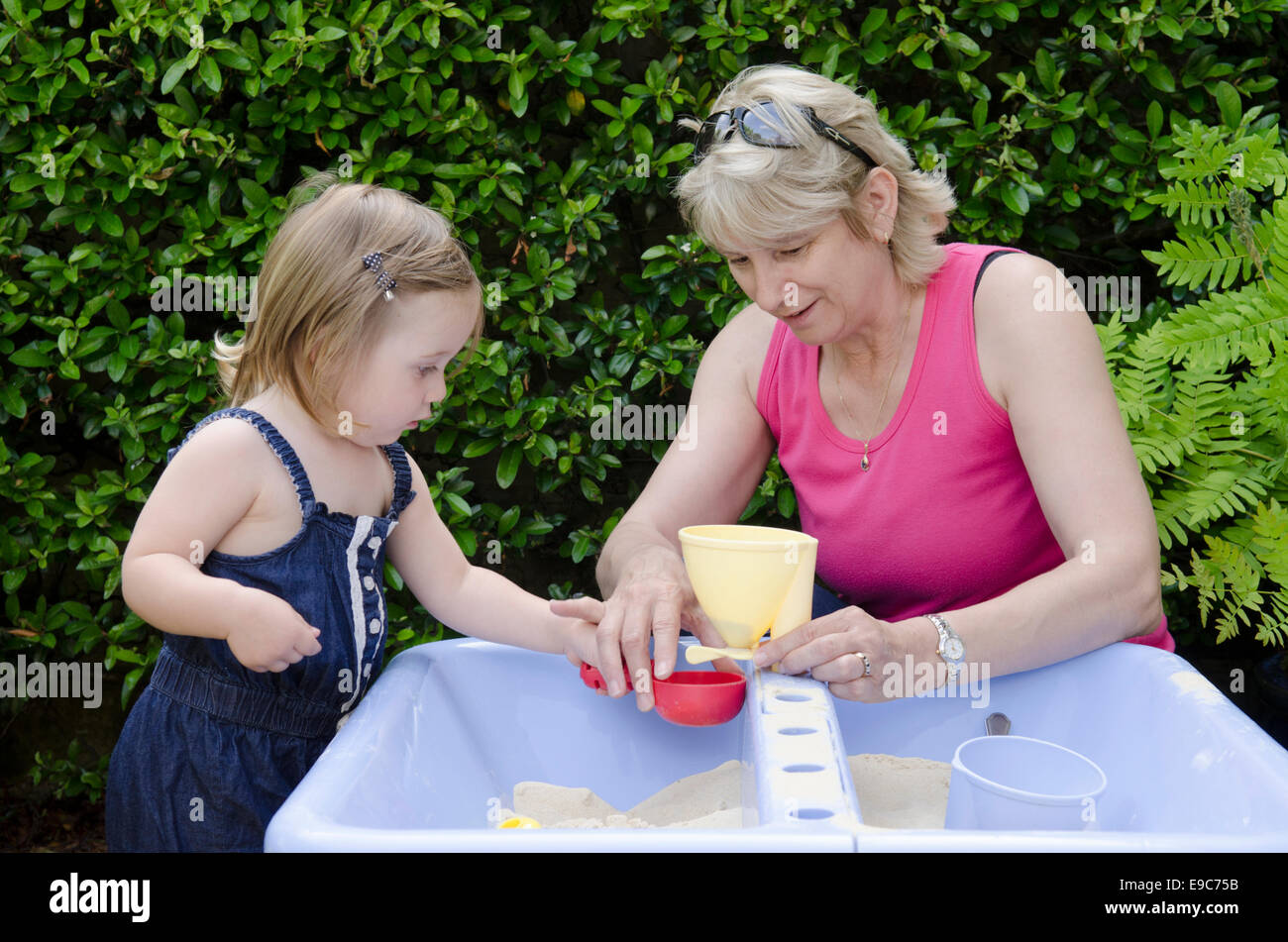 Grandmother playing in sandpit with granddaughter. UK Stock Photo