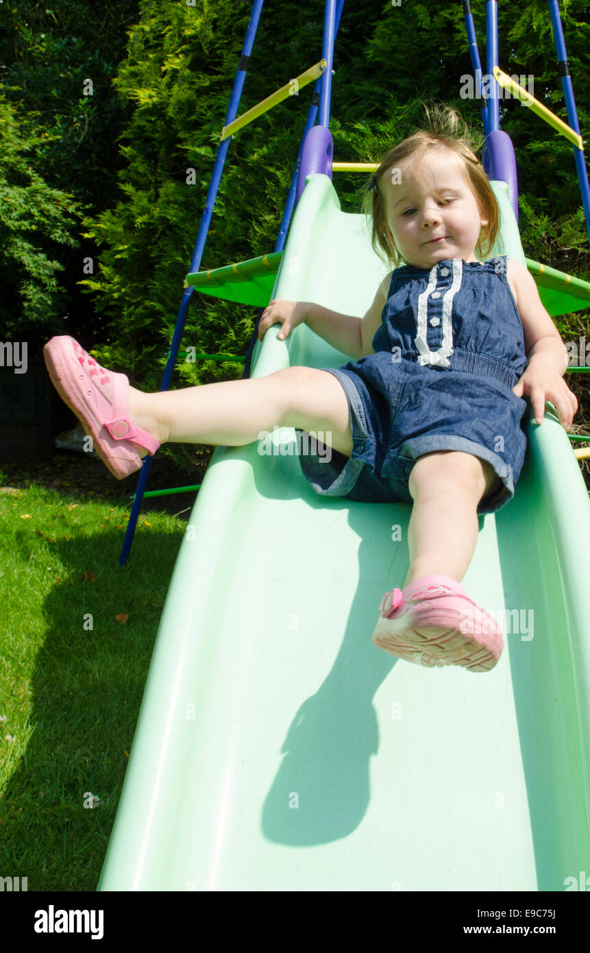 Two year old girl on slide climbing frame in garden. UK Stock Photo